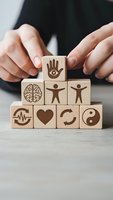 Hands protecting wooden blocks with wellness symbols including brain, heart, yin yang and human figures representing holistic health and mental wellbeing concepts.