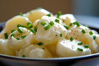 Freshly boiled potatoes garnished with chopped chives and black pepper served in rustic bowl, close up view of traditional homestyle cooking.