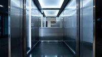 Modern elevator interior with stainless steel walls and glass panels featuring contemporary lighting design for commercial building transportation systems.