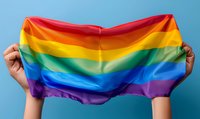 Hands holding up colorful rainbow pride flag against blue background, symbolizing LGBTQ+ community support, equality, and celebration of diversity.