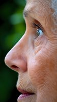 Close-up profile view of senior woman's face showing bright blue eye, natural wrinkles, and gentle expression against blurred green background, suitable for aging concepts.