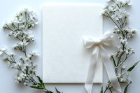 White blank card with elegant satin bow and delicate baby breath flowers creating romantic border on light background, perfect for wedding invitations.