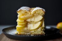 Layered apple cake slice with tender fruit filling and golden pastry on dark plate, homemade dessert ready for bakery menu or recipe blog content.