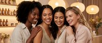Four diverse women friends laughing together in cozy restaurant setting with warm lighting. Perfect for friendship, dining, social media content.