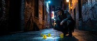 Male detective examining crime scene evidence markers in dark urban alley at night. Professional investigator crouched down analyzing clues under streetlight.