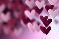 Pink and burgundy paper hearts floating on blurred romantic background with soft bokeh effect, creating dreamy Valentine's Day atmosphere for greeting cards and celebrations.