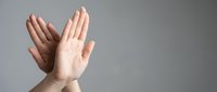 Two hands pressed together in prayer or meditation gesture against neutral gray background for wellness and spirituality concepts.