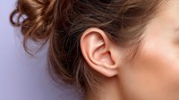 Close-up of female ear and side profile showing brown hair against purple background, highlighting facial anatomy for medical or beauty concept.