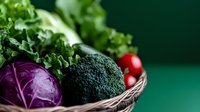 Fresh organic vegetables in woven basket including purple cabbage, broccoli, lettuce and cherry tomatoes on green background, healthy eating concept.