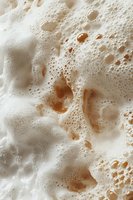 Creamy coffee foam macro with delicate bubbles and swirls in shades of white and caramel brown, creating abstract patterns and textures for food photography.