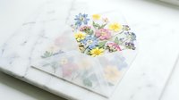 Colorful floral heart sticker on white paper with scattered flower petals, craft supplies for scrapbooking and DIY projects on clean workspace.