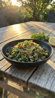 Tabbouleh salad with fresh herbs, tomatoes, and quinoa served in black bowl on wooden outdoor table with lemon slice and garden backdrop.