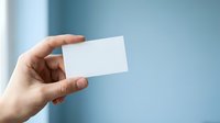 Hand holding blank white business card against blue wall background for corporate branding and professional identity mockup.