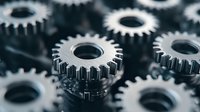Metallic gears in motion create industrial machinery pattern, close-up view shows mechanical engineering components with precise interlocking teeth in dark tones.
