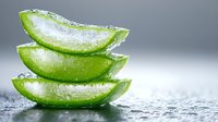 Fresh aloe vera plant slices stacked with water drops on gray background, showing translucent gel texture for natural skincare and wellness concepts.