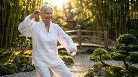 Senior man practicing tai chi in bamboo garden at golden hour, wearing white clothing, demonstrating martial arts exercise outdoors.