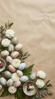 Easter eggs in pastel colors with white ranunculus flowers and green foliage arranged on beige fabric background with copy space for spring holiday design.