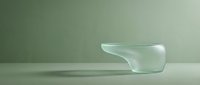 Minimalist transparent glass bowl with smooth organic curves on a soft sage green background, casting subtle shadows on a light surface.
