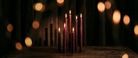 Elegant burgundy candles burning with warm flames on rustic wooden surface against dark background with golden bokeh lights creating cozy atmospheric ambiance.