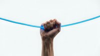 Hand gripping blue rope or cable in tug of war position against white background. Strength, determination, teamwork and competition concept.