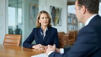 Professional businesswoman in navy suit during corporate meeting with male colleague in modern office conference room for business consultation.