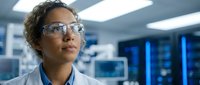 African American female scientist wearing safety glasses and lab coat in modern research laboratory with blue lighting and equipment.