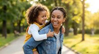 Happy African American mother and daughter embracing outdoors in sunny park during golden hour family bonding moment for lifestyle and parenting concepts.