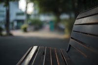 Wooden park bench with shallow depth of field creating bokeh effect in urban setting with blurred background for relaxation and outdoor lifestyle concepts.