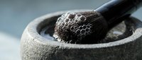 Black truffle in stone mortar with pestle for gourmet cooking and culinary preparation on neutral background.