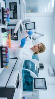 Female scientist with blonde hair, Caucasian ethnicity, wearing white lab coat and blue gloves, conducting genetic analysis in modern laboratory with DNA sequencing equipment, colorful sample tubes, and digital displays for research and medical testing.