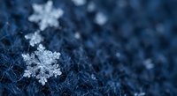Delicate snowflakes rest on dark blue winter fabric surface creating magical seasonal atmosphere for holiday decorations and festive designs.