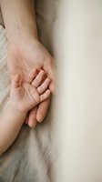 Adult and child hands gently touching in tender moment showing family bond, care and protection on soft neutral fabric background for emotional concepts.