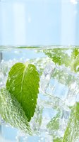 Fresh mint leaves and ice cubes splashing in crystal clear water creating refreshing summer drink with bubbles and droplets for beverage photography.