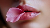 Pink rose petal resting on natural glossy lips in artistic macro photography, representing beauty, sensuality and natural cosmetics for advertising and design.