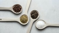 Wooden spoons filled with assorted spices and seasonings arranged on light textured surface for culinary cooking and food preparation projects.