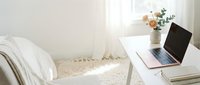 Minimalist white bedroom workspace with laptop on desk, soft natural lighting, clean modern interior design for remote work and productivity.