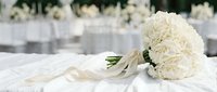 Elegant white peony bridal bouquet with silk ribbon on marble table at luxury wedding reception venue with soft bokeh background for romantic ceremonies.