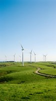 Wind turbines scattered across rolling green hills with winding road, clear blue sky. Renewable energy and sustainable power generation for environmental and industrial projects.