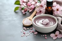 Pink clay face mask in bowl with cherry blossoms, essential oil and spa accessories for natural skincare and beauty treatment routine.