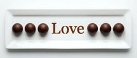 Chocolate truffles arranged around the word Love on a white ceramic plate, isolated on white background, for Valentine's Day and romantic designs.
