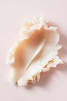 Delicate cream-colored seashell on soft pink background showcases natural curves and textures with gentle shadows creating ethereal, dreamy atmosphere.