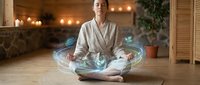 Young woman meditating in lotus position with glowing energy aura effects in cozy spa interior with warm lighting and plants for wellness concepts.