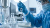Medical researcher in protective equipment conducting laboratory experiment with pipette and petri dish in sterile clinical environment for scientific research.