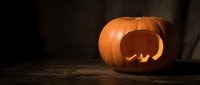 Glowing carved pumpkin jack-o-lantern with spooky face on rustic wooden surface against dark background for Halloween celebration and autumn decor.