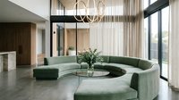 Spacious modern living room with curved green sectional sofa, round glass coffee table, pendant lighting, floor-to-ceiling windows, and minimalist decor for contemporary home design.