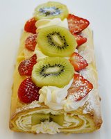 Fresh fruit strudel with sliced kiwi, strawberries and whipped cream on flaky puff pastry, dusted with powdered sugar against white background.