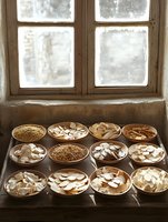 Ceramic bowls filled with dried mushroom slices arranged on wooden windowsill, natural light streaming through frosted window creates moody atmospheric food photography.