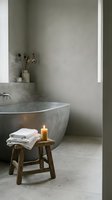 Minimalist spa bathroom with concrete bathtub, wooden stool holding folded towels and burning candle, dried flowers in vase on shelf, neutral tones, natural light from window.