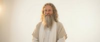 Serene elderly Caucasian man with long gray beard and hair in flowing white robes standing peacefully against soft luminous background for spiritual content.