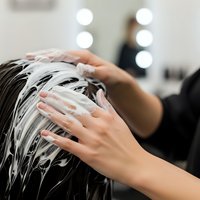 Professional hair washing treatment with shampoo foam at modern salon with mirror lights for haircare and beauty services.